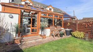 A house with a conservatory, a wooden deck, and a garden. - Beckside Cottage (Penrith)