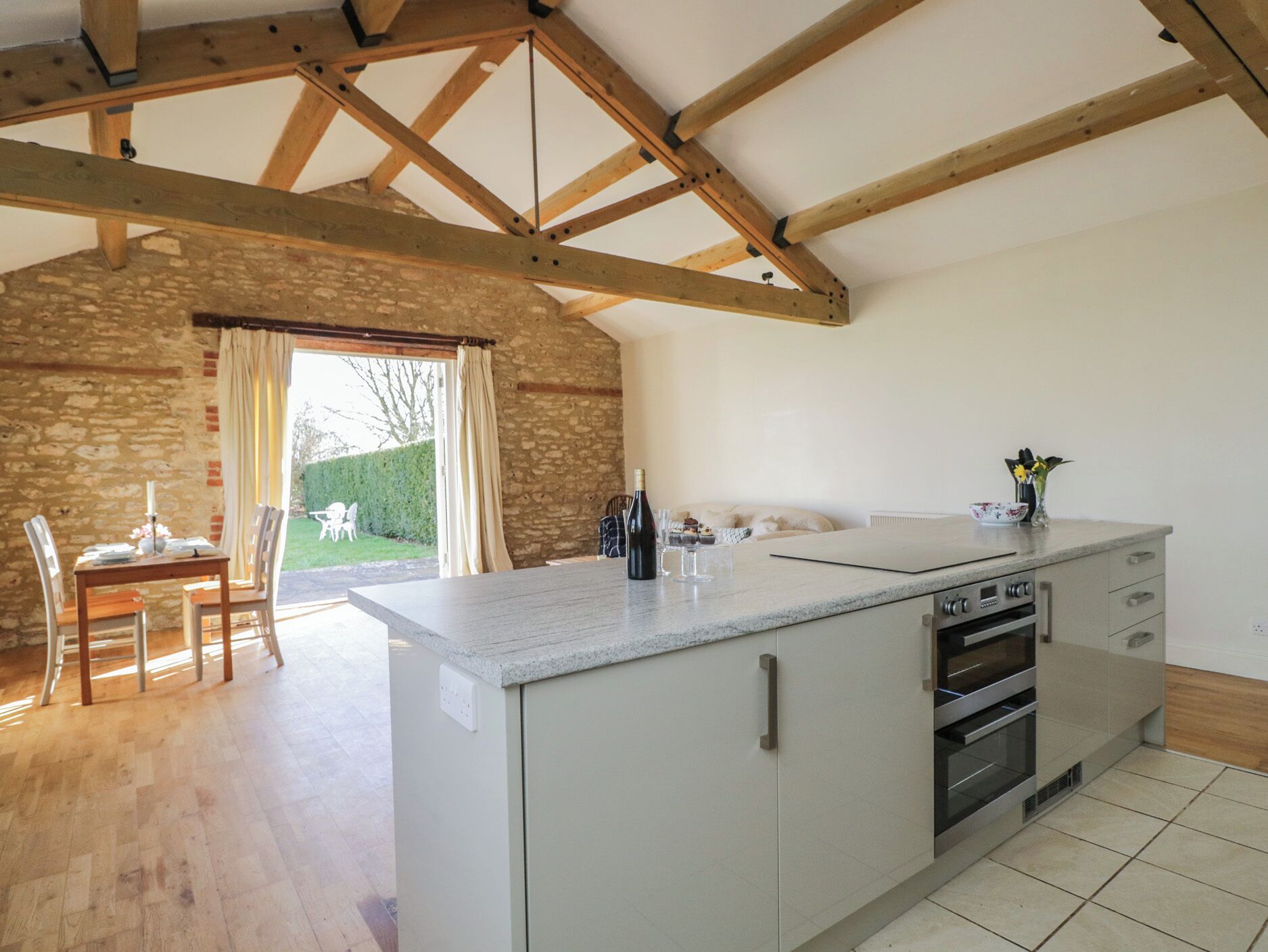 A kitchen with a large island, wooden beams, stone walls, and a dining area with a table and chairs.