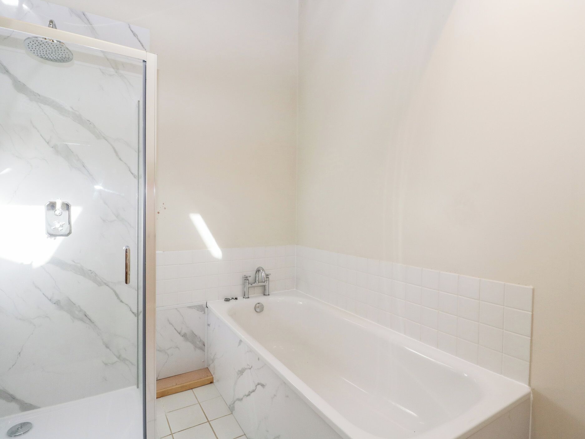 Un baño con ducha acristalada, una bañera independiente y paredes de mármol blanco.