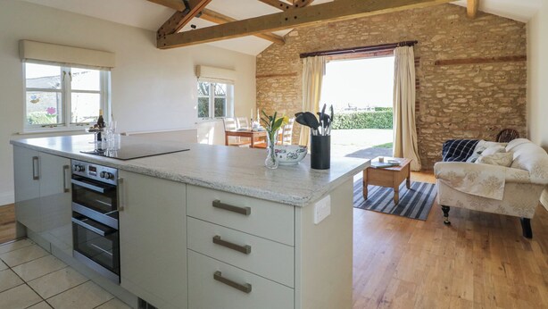 A kitchen with a central island, built-in oven, and a dining area with a table and chairs. - South Barn Cottage (Faringdon)