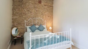 A bedroom with a stone wall, a white metal bed frame, and a bedside table with a mirror. - South Barn Cottage (Faringdon)
