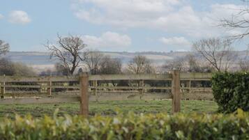 A rural landscape with a wooden fence, open fields, and distant hills under a partly cloudy sky.