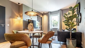 A modern living room with a dining area, featuring a round table, cushioned chairs, a large potted plant, and a sofa.