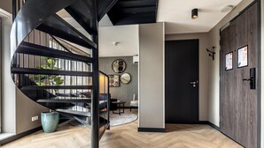 A modern interior with a spiral staircase, wooden flooring, a dark door, and a wall-mounted light fixture.