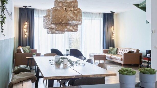 A modern living room with a wooden dining table, two sofas, and a large window with curtains. - Waterfront Holiday Home with Terrace Views (Stavoren)