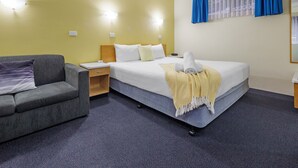Une chambre d’hôtel avec un lit, un canapé gris, une table de chevet et une fenêtre avec des rideaux bleus.