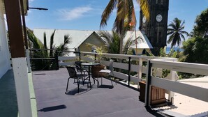 A balcony with a table and chairs, a clock tower, and palm trees in the background.