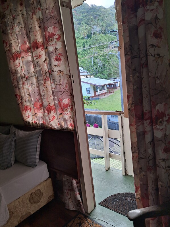 Una habitación con una cama, una silla de madera y vistas a una casa y follaje exterior.