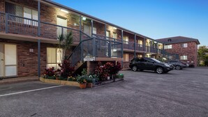Un motel avec une façade en briques, une allée couverte et un parking rempli de voitures.