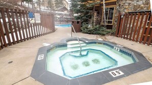 A hot tub with a tiled edge and a metal ladder, surrounded by a wooden fence and a stone building.