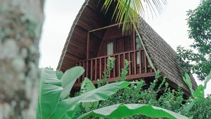 A wooden house with a thatched roof surrounded by lush greenery.