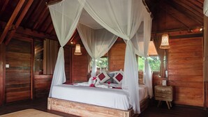 A wooden four-poster bed with white linens and red pillows, a wooden nightstand, and a woven lamp.