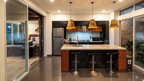 Une cuisine moderne dotée d’un îlot central, de tabourets de bar et de luminaires suspendus.