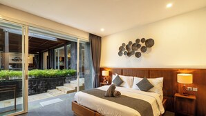 Une chambre d’hôtel moderne dotée d’un grand lit, de deux tables de chevet avec des lampes, d’un élément décoratif fixé au mur et d’une porte-fenêtre coulissante donnant sur un espace extérieur agrémenté de plantes.