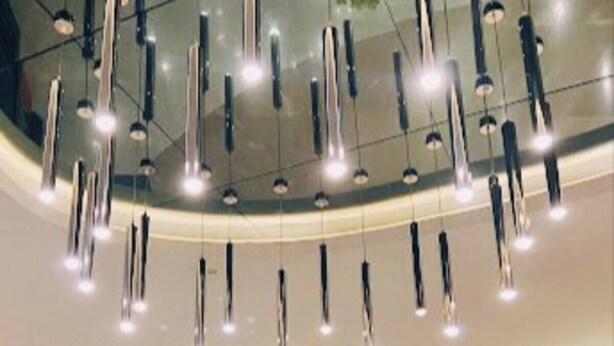 A modern lobby with a circular seating area, hanging pendant lights, and a central chandelier.