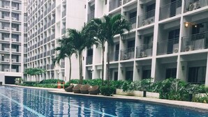 A swimming pool with clear blue water, surrounded by a modern building with balconies and palm trees.