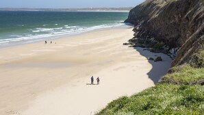 Una playa con un acantilado rocoso en un lado y un cielo azul despejado.