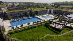 Un hotel moderno con piscina en la azotea, asientos exteriores y vistas a la vegetación circundante.