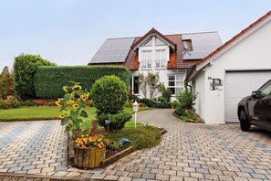 Una casa con camino de entrada pavimentado, garaje y un jardín bien cuidado con flores y arbustos.