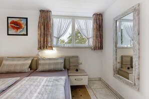 Un dormitorio con cama, una mesita de noche, un espejo, una ventana con cortinas y una obra de arte colgada en la pared.