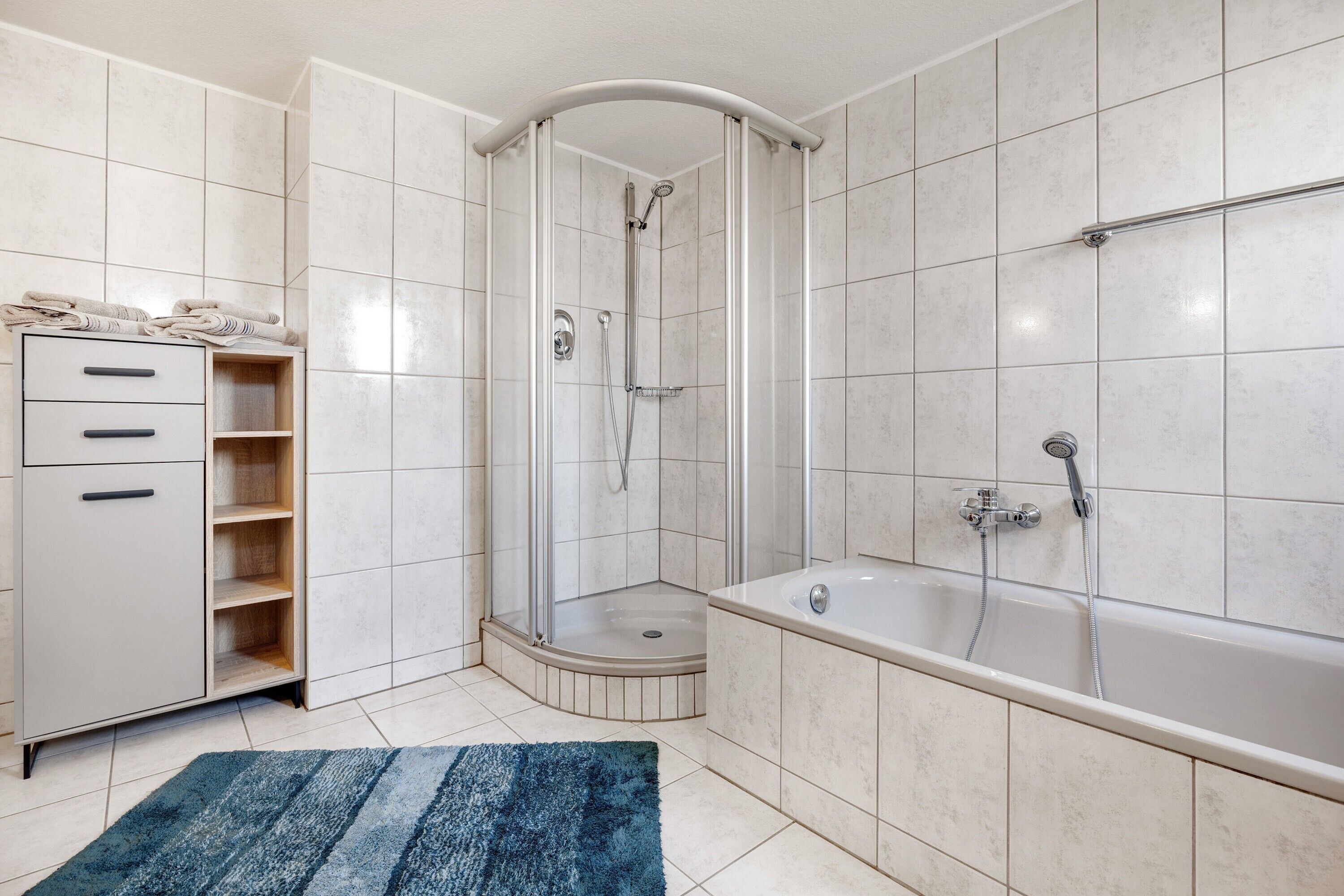 Un baño moderno con ducha de vidrio, bañera independiente y un armario empotrado con estantes abiertos.
