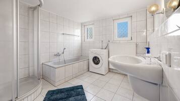 Ein modernes Badezimmer mit Dusche, Badewanne, Waschmaschine und Waschbecken.