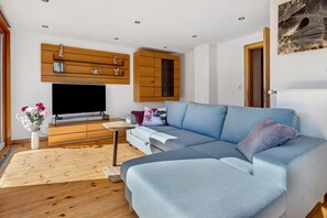 A modern living room with a sectional sofa, a flat-screen TV, wooden cabinets, and a decorative vase with flowers.