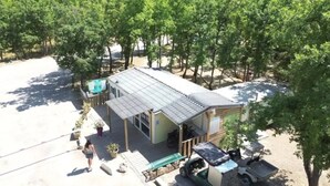 A small, single-story building with a sloped roof, surrounded by trees. There is a paved area with a bench and a small table. - ZEcamping 3* chiens acceptés mobil-home clim 28m2 6 pers (Bauduen)