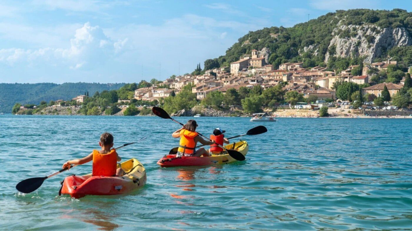Tres kayaks sobre un lago tranquilo con un pueblo al fondo.