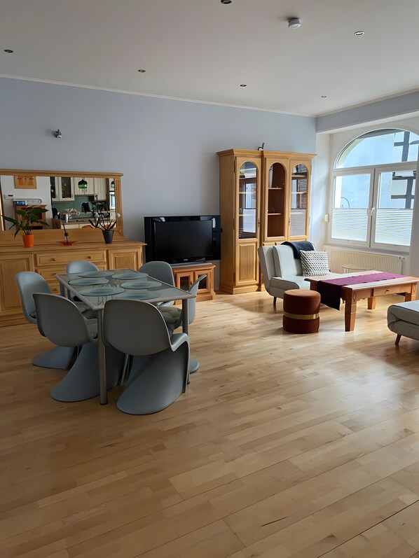 A modern living room with a dining area, a TV, and a large window.