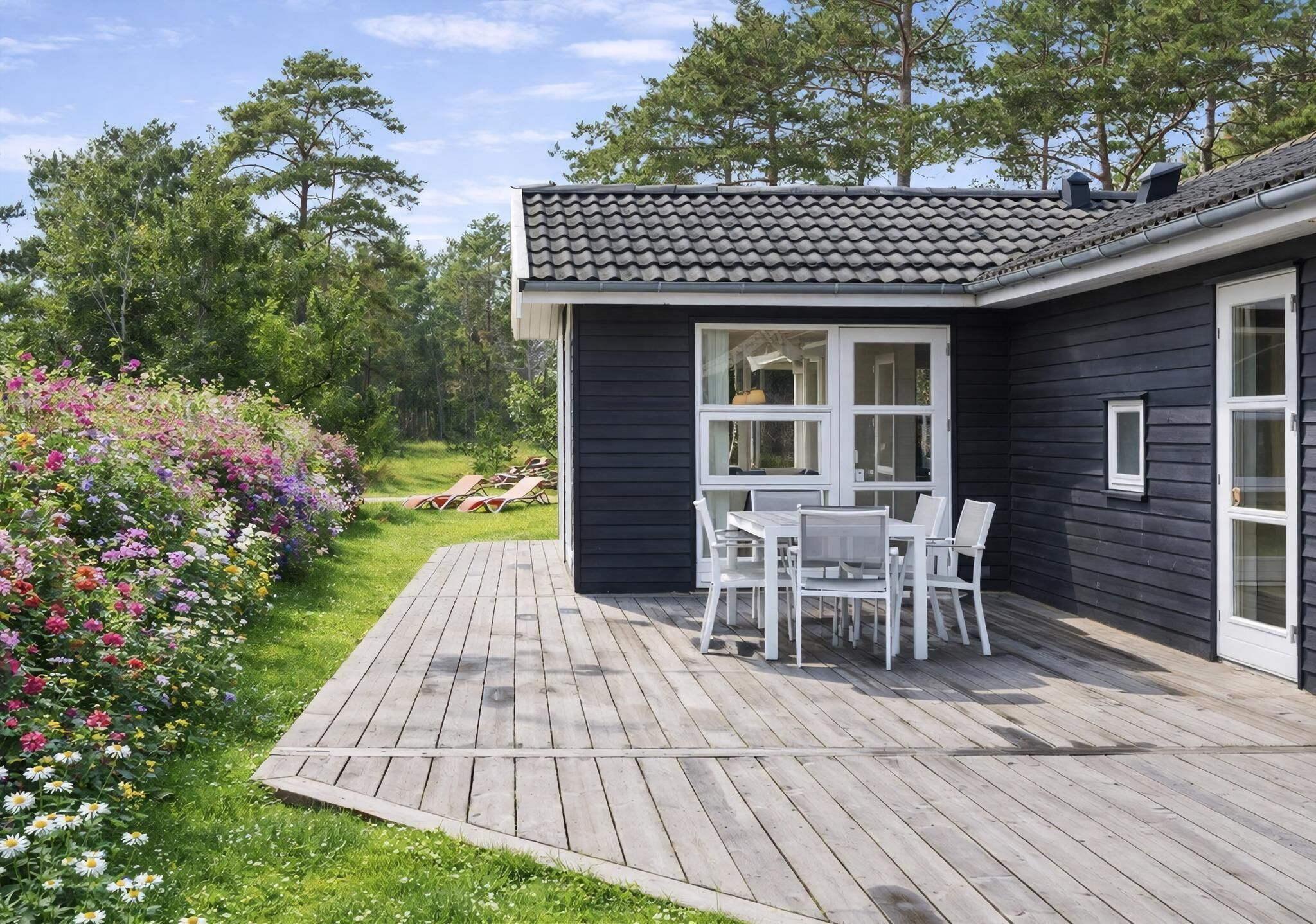 Una casa con terraza, comedor con sillas y jardín con flores.