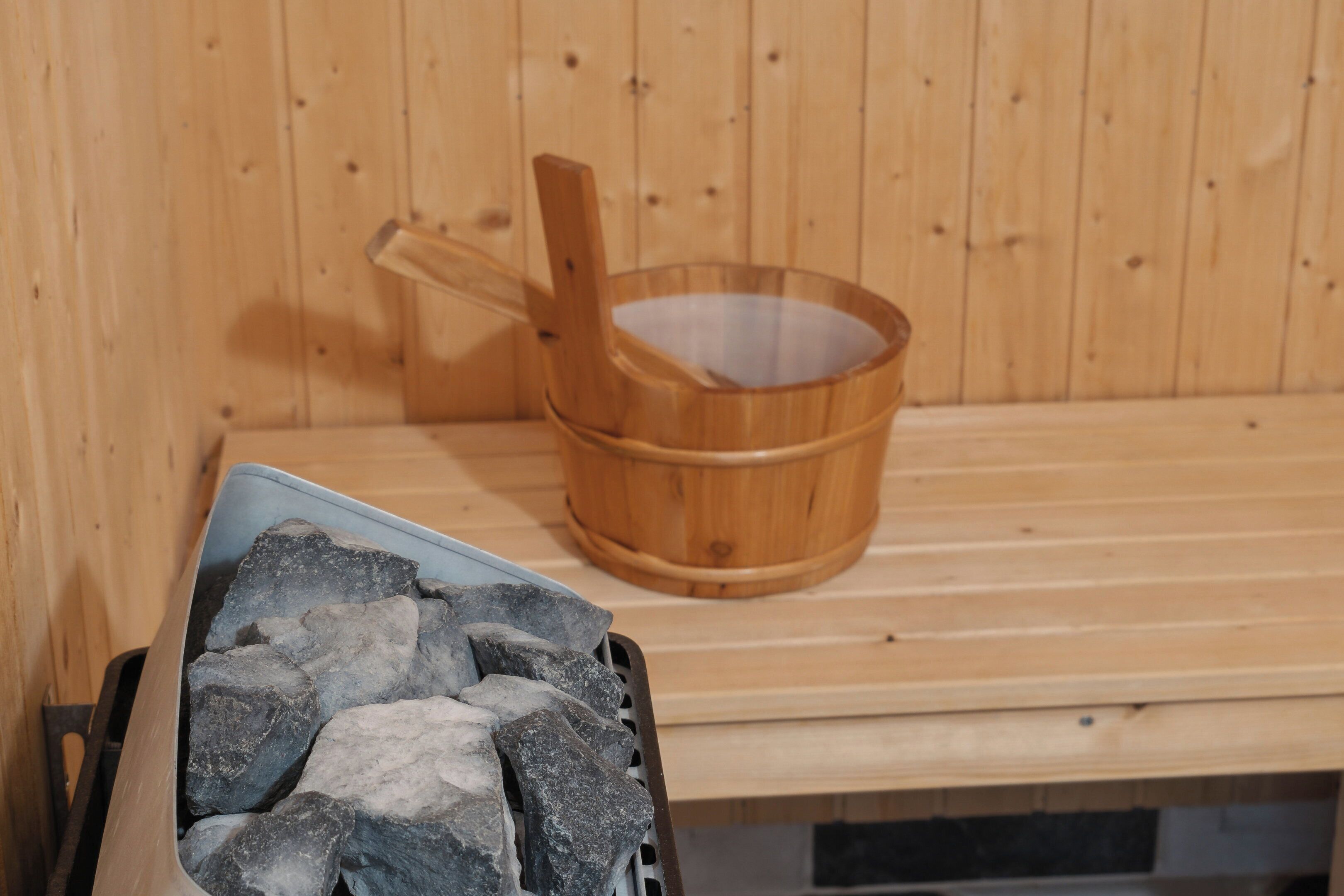 Een sauna met een houten bank, een houten emmer en een bak met stenen.