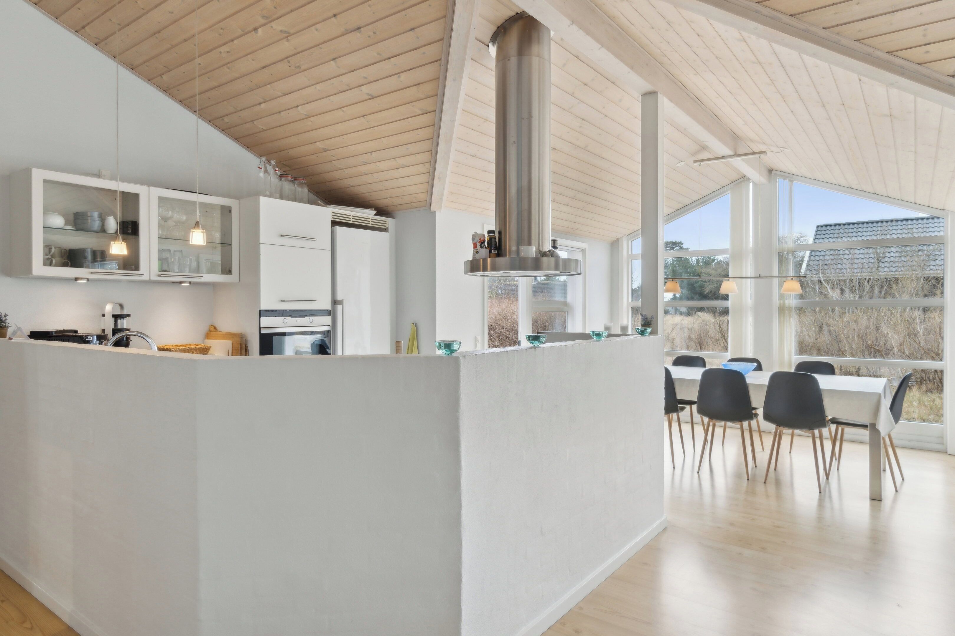 A modern kitchen with a central island, white cabinetry, and a dining area with a large window.