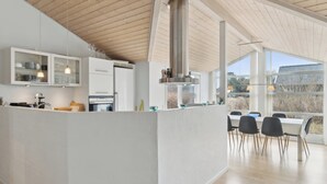 Une cuisine moderne dotée d’un îlot central, de meubles blancs et d’un coin repas avec une grande fenêtre.
