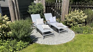 A circular patio with two white lounge chairs and a small table, surrounded by greenery and a wooden fence. - Apartment 'Kleine Mügge' with Private Terrace, Private Garden and Wi-Fi (Zingst)