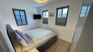 A compact bedroom with a bed, bedside table, and a TV mounted on the wall. - Apartment 'Kleine Mügge' with Private Terrace, Private Garden and Wi-Fi (Zingst)