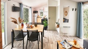 A modern kitchen with a dining area, a TV mounted on the wall, and a view of the outdoors. - ZEcamping 3* dog friendly mobil-home TV clim 29m2 5 pers (Bauduen)
