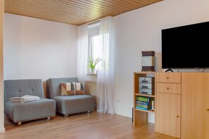 Moderni olohuone, jossa on kaksi harmaata sohvaa, puinen kaappi, jossa on elektronisia laitteita, ja suuri televisio.