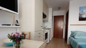 A narrow hallway leading to a bedroom with a bed, a small kitchenette, and a bathroom visible in the background.