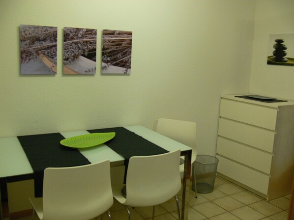 A small dining area with a table, two chairs, a green placemat, and a trash can.