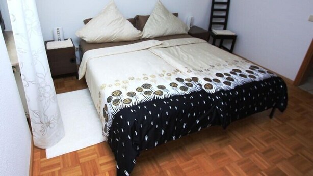 Un dormitorio con cama, mesitas de noche, una silla, una obra de arte en la pared y suelo de madera.