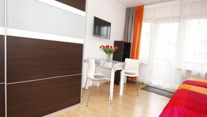A hotel room with a bed, a desk with a chair, a TV mounted on the wall, and a window with curtains. - Studio 'Falk Wohnung Nr -3-' with Mountain View, Balcony and Wi-Fi (Freiburg im Breisgau)