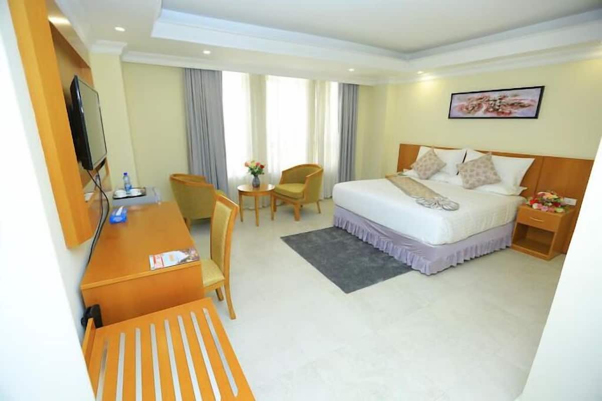 A hotel room with a bed, a desk, a chair, a TV, and a painting on the wall.