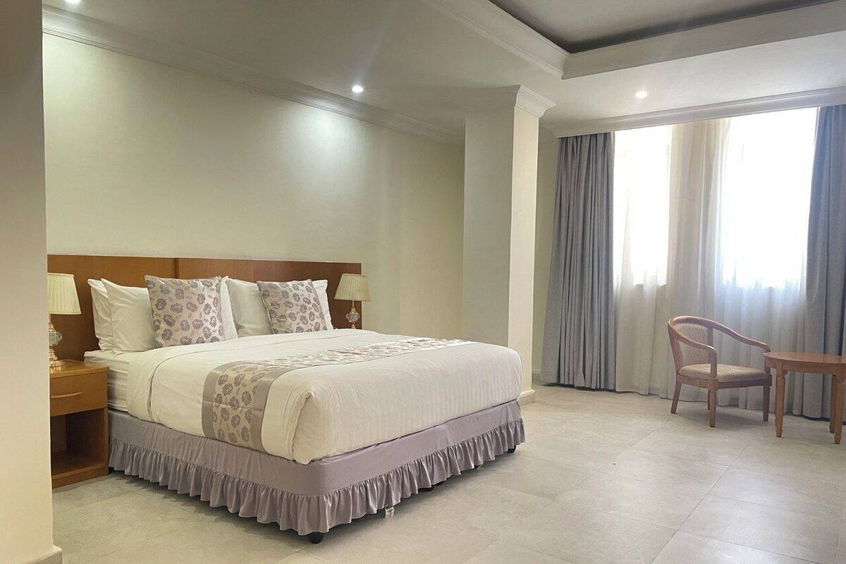 A hotel room with a large bed, a wooden nightstand, a chair, and a table.