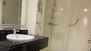 Een moderne badkamer met een wit wastafel, een zwart aanrecht en een douchecabine met glazen wanden.