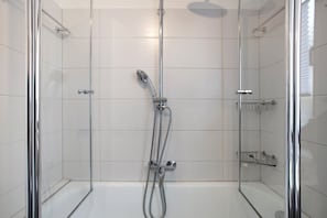 A glass-enclosed shower with a handheld showerhead and a fixed overhead showerhead.