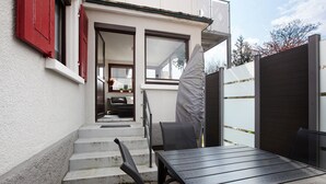 Une terrasse avec une table et des chaises, un espace abrité et une vue sur l’intérieur grâce à une porte vitrée.