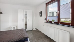 Une chambre à coucher avec un lit, une armoire blanche, un radiateur et une fenêtre avec des stores.