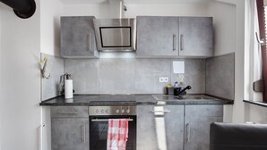 Une cuisine moderne avec des meubles gris, une hotte en acier inoxydable, un four encastré et une fenêtre avec des rideaux.