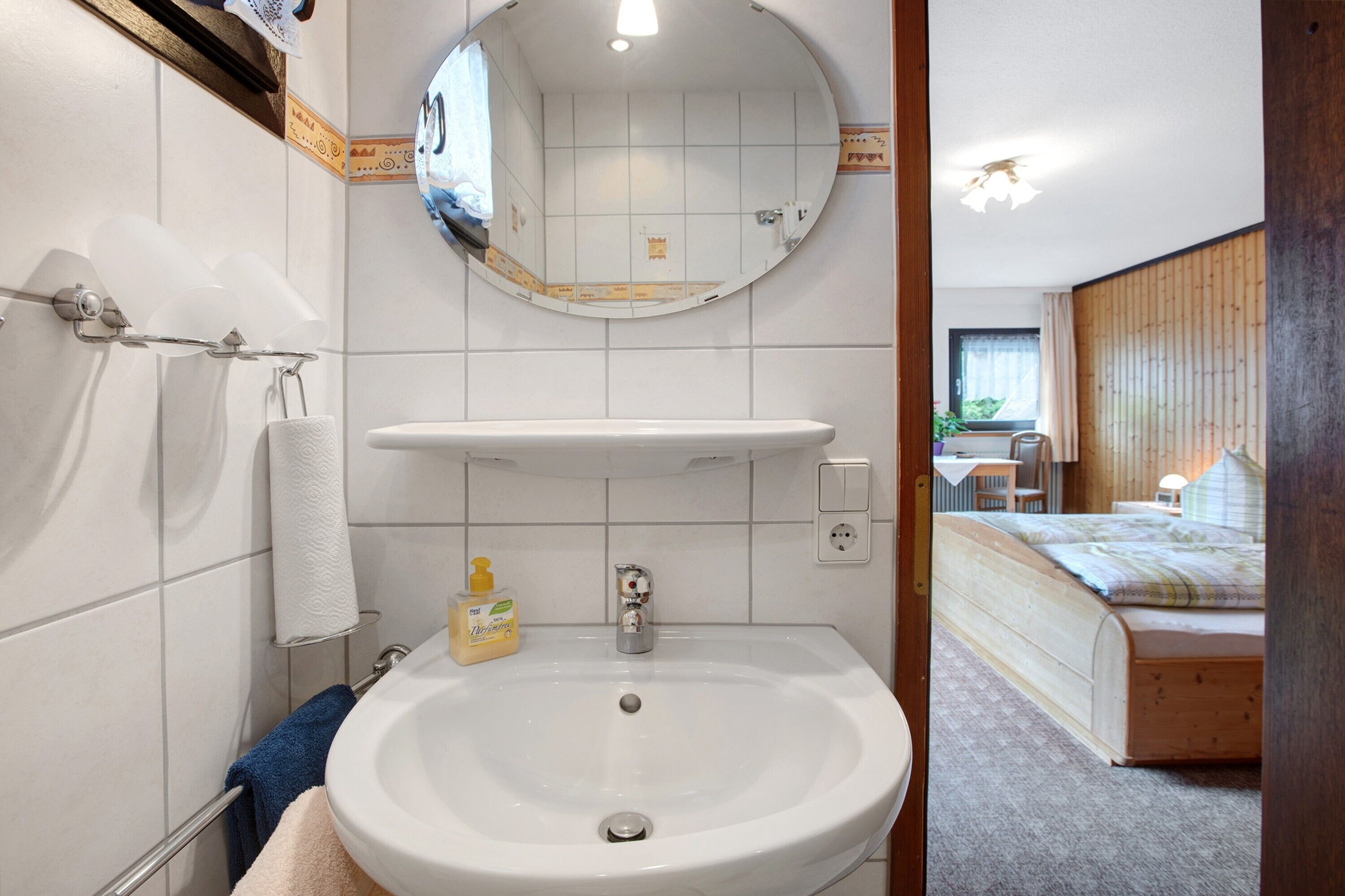 A bathroom with a sink, mirror, towel rack, and toilet paper holder.